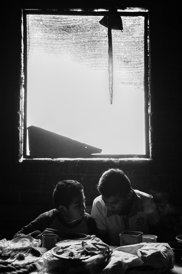 Two brothers converse over a meal. Tamazulapam del Espiritu Santo, Oaxaca, Mexico.