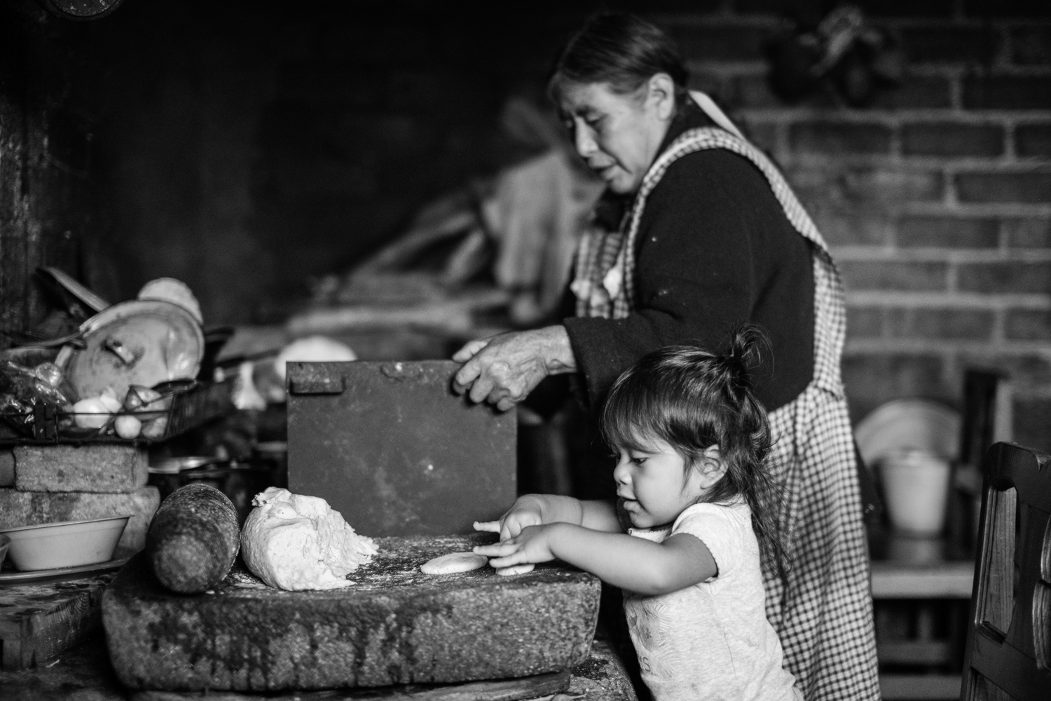 A grandmother passes on tortilla technique to her granddaughter. Tamazulapam del Espiritu Santo, Oaxaca, Mexico.